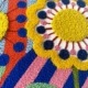 Tableau textile brodé représentant trois grandes fleurs stylisées sur un fond de motifs arlequin colorés et géométriques, réalisé en punch needle