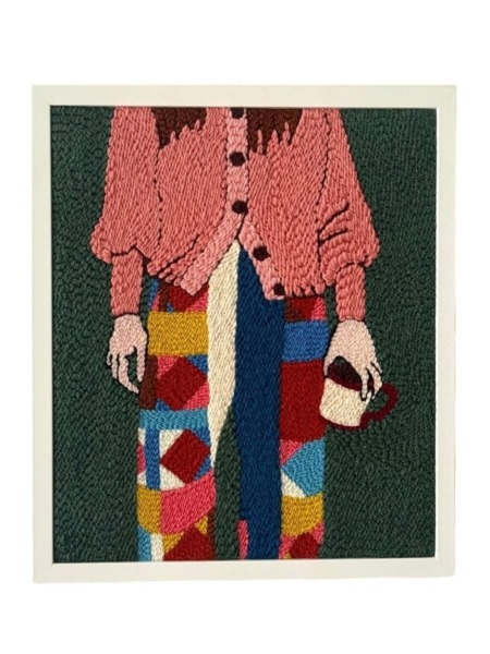 Tableau brodé représentant une silhouette féminine en pantalon patchwork et gilet rose, réalisé à la main en punch needle.