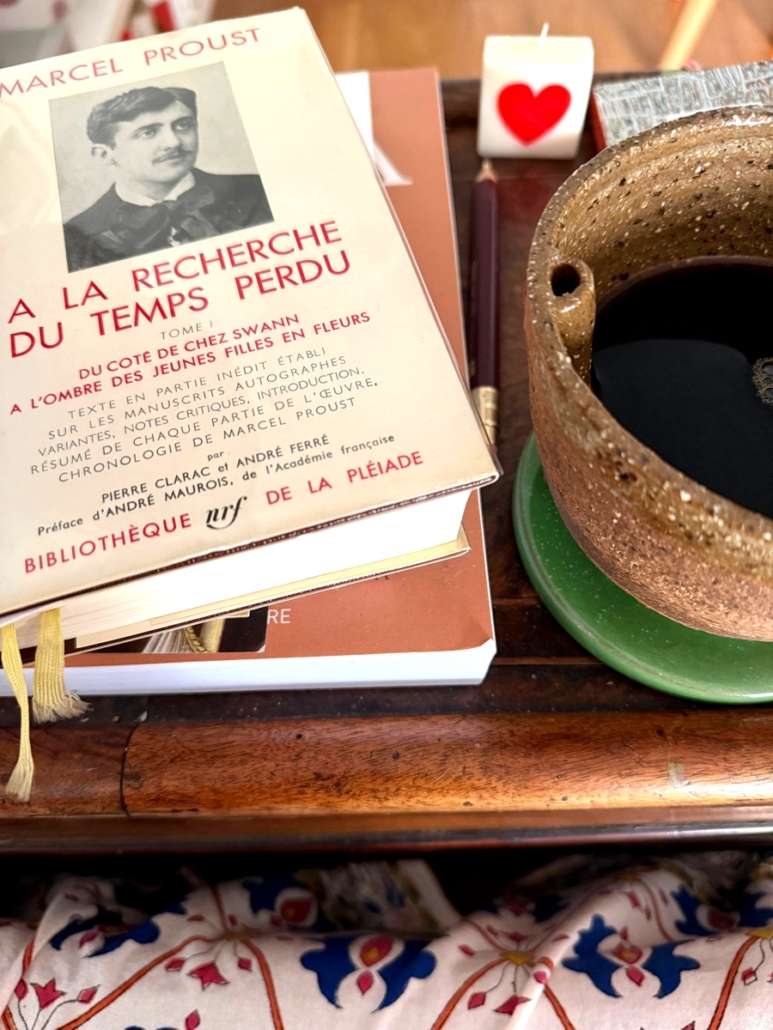 Édition de À la recherche du temps perdu de Marcel Proust, posée sur une table en bois à côté d'un bol en céramique.