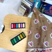 Deux boîtes de pastels aux couleurs vives posées sur une table en bois, à côté d'un tissu à motifs floraux dans l'atelier d'Agnès Pironon.